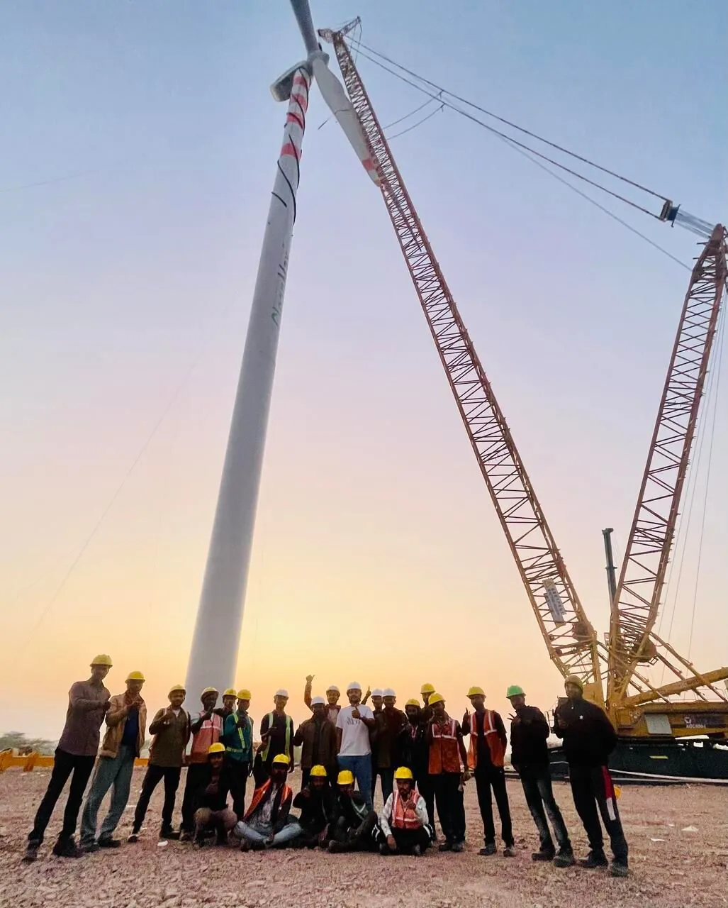 Greentech team at sunset beside a crane and wind turbine tower